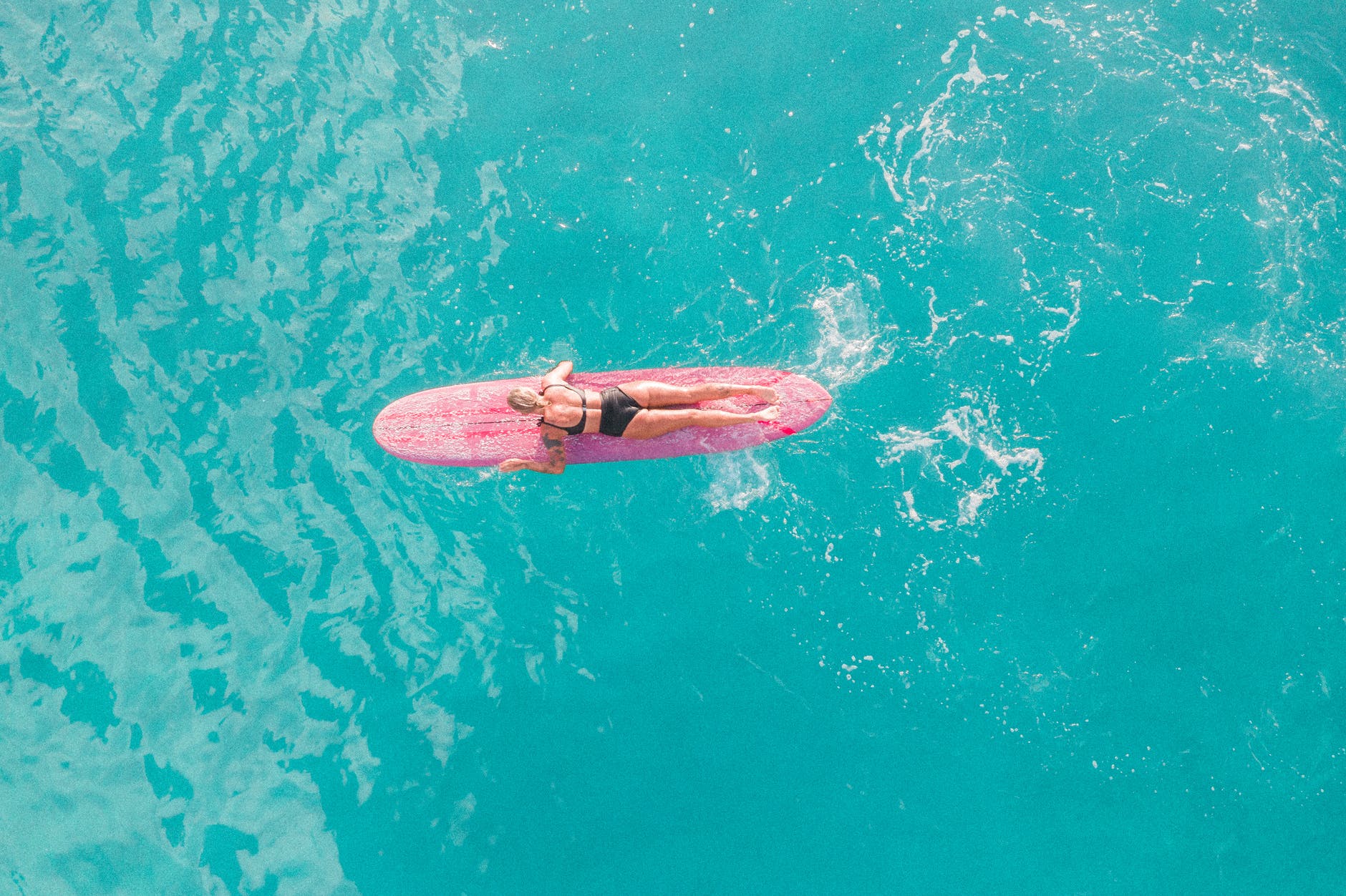 woman in pink and white bikini lying on pink surfboard on water